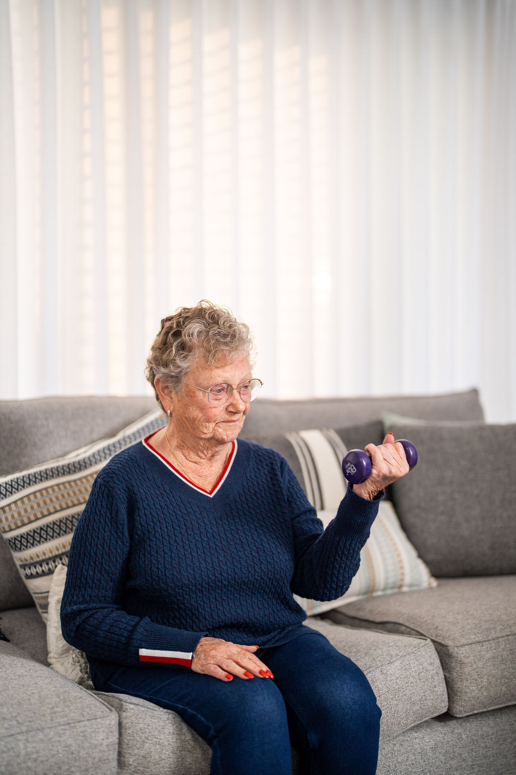 Older woman doing a seated dumbbell exercise on her lounge at home